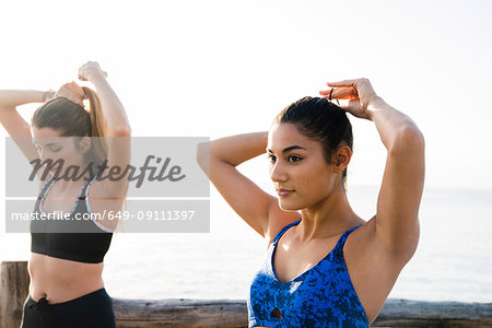 Two young women training on beach, tying hair ponytails