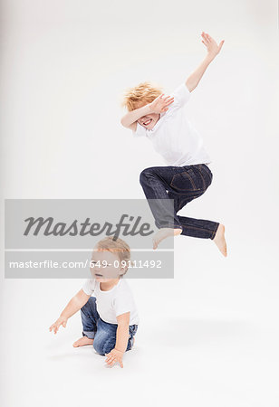 Portrait of boy leaping in air over baby brother