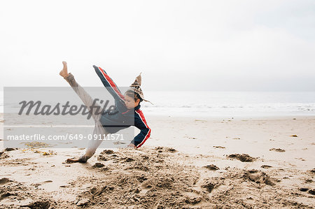 Young boy on beach, practising martial arts, leg raised in kick
