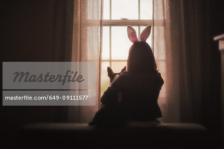 Girl, sitting with dog, in front of window, rear view