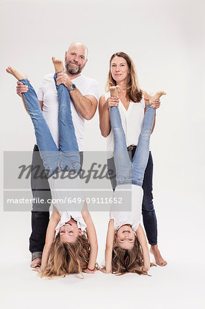 Studio portrait of mature couple with two daughters doing hand stands, full length