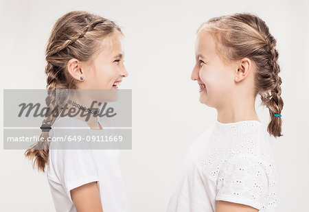 Studio portrait of two girls with hair plaits face to face, head and shoulders