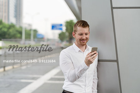 Young businessman looking at smartphone touchscreen in city, Shanghai, China