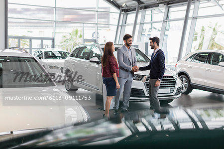 Car salesman and customers handshaking in car dealership showroom