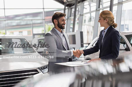 Car saleswoman and male customer handshaking in car dealership showroom