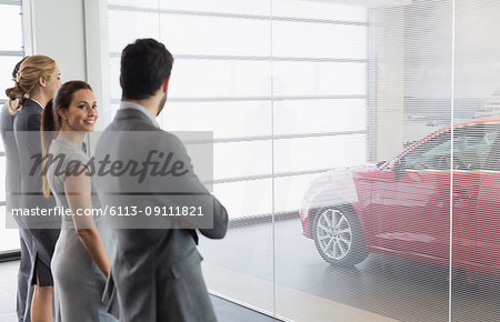 Car sales people looking at new, red car in car dealership showroom