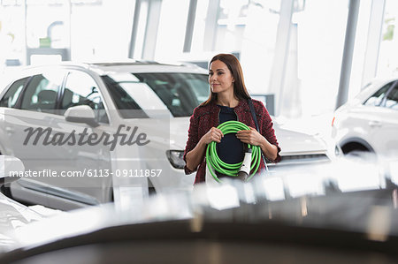 Female customer carrying hybrid charging cord in car dealership showroom