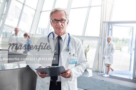 Portrait confident senior male doctor with clipboard in hospital lobby