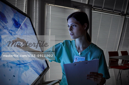 Serious female nurse using touch screen computer monitor, viewing microscope slide