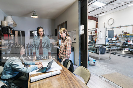 Three women gathered around table in office area of a metal workshop.