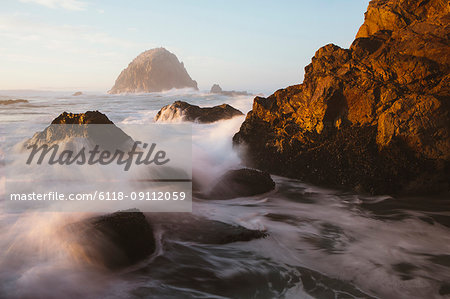 Seascape with breaking waves over rocks at dusk.