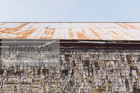 An old farmhouse with wooden shingle tiles on the walls and corrugated iron roof. Silvery grey colours.