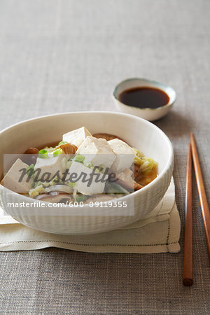 Tofu in broth with shiitake mushrooms, green onions and cabbage served with soy sauce and chopsticks