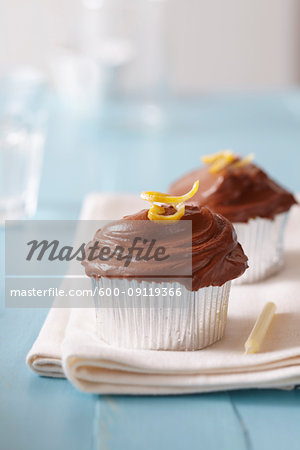 Chocolate frosted cupcakes with lemon zest and a candle on a blue background