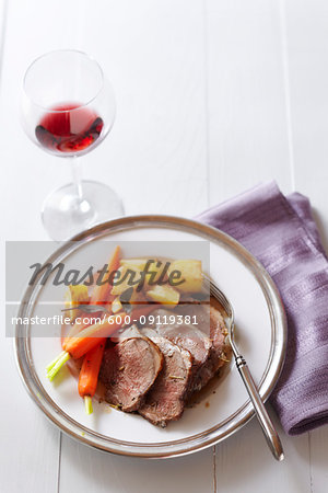 Dinner plate of lamb with carrots, potatoes and a glass of red wine with a purple napkin