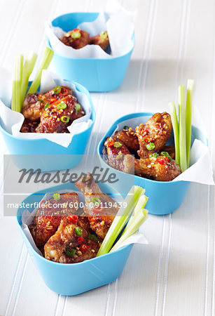 Chicken wings covered in chili and scallion sauce in blue bowls with celery sticks