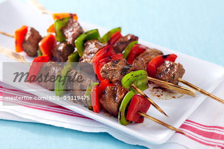 Grilled steak and pepper skewers on a platter with red striped napkin