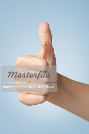 Female thumb with adhesive bandage on blue background