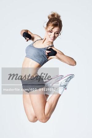 Young woman jumps while making aerobics exercises on gray background