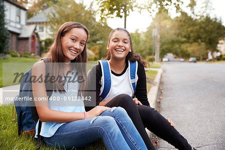 Two teen girlfriends sit at the roadside looking to camera