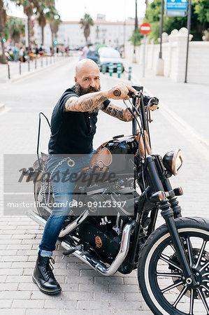 Portrait of mature male hipster astride motorcycle, Valencia, Spain