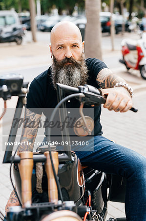 Portrait of mature male hipster astride motorcycle in parking lot