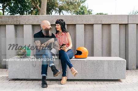 Tattooed mature hipster couple sitting on concrete bench