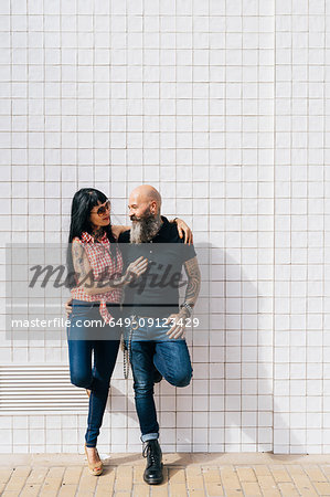 Mature hipster couple leaning against white wall