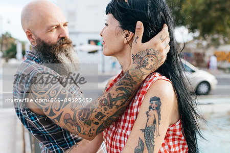Mature tattooed hipster man with hand in girlfriend's hair