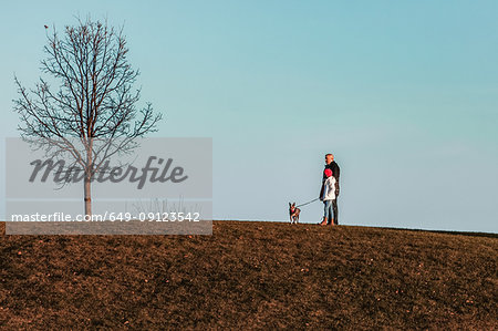 Father and daughter walking dog on hillside