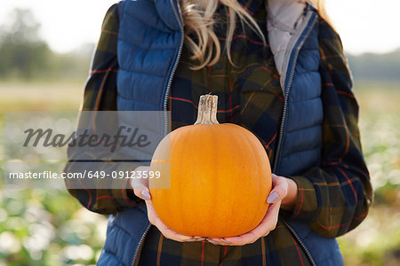 Mid section of woman holding pumpkin in pumpkin patch field
