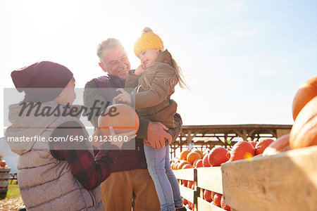Girl and brother with grandfather selecting pumpkins in pumpkin patch field