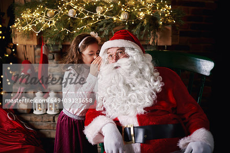 Young girl visiting Santa, whispering into Santa's ear