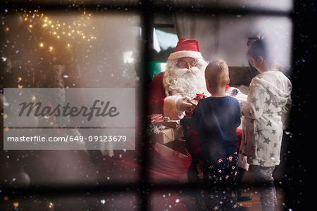 Young girl and boy receiving gifts from Santa, viewed through window