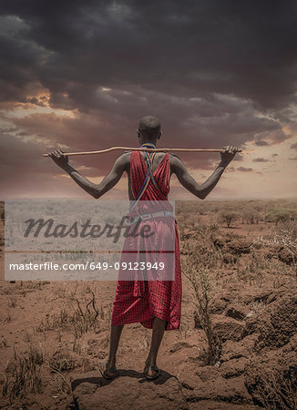 Masai man with traditional dress watching stormy clouds over the savannah, Amboseli, Rift Valley, Kenya