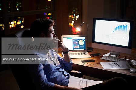 Young businessman staring at computer on office desk at night