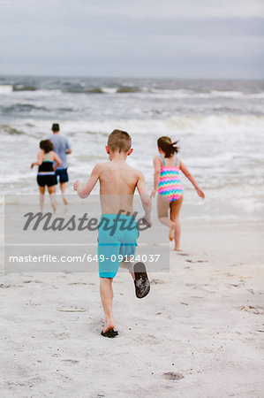 Man and children running toward sea from beach, rear view, Dauphin Island, Alabama, USA