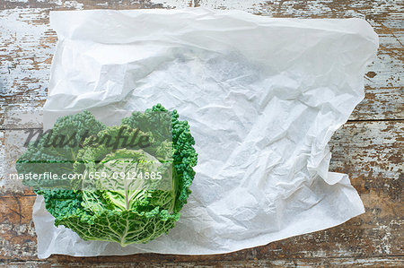 A savoy cabbage on paper and a wooden background (top view)