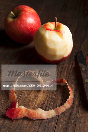 Two whole apples, one peeled, and a heart made out of the peelings