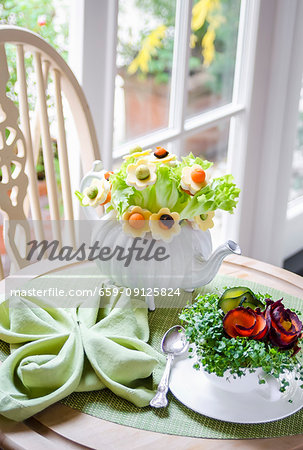 Bouquet of salad leaves and flowers made with cheese, carrots and avocado in a teapot, watercress and carrots in a tea cup on a green tablemat