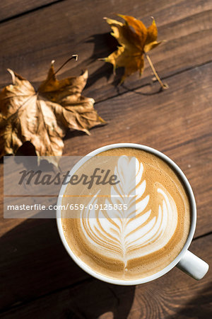 Flat white, cappuccino coffee with rosetta or florette latte art on a wooden background with autumn leaves Flat white, cappuccino coffee with rosetta or florette latte art on a wooden background with autumn leaves
