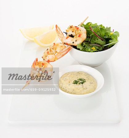 Grilled prawns on a skewer with chilly and pepper, bowl of mixed lettuce, Lemon wedges and tartare sauce with dill topping