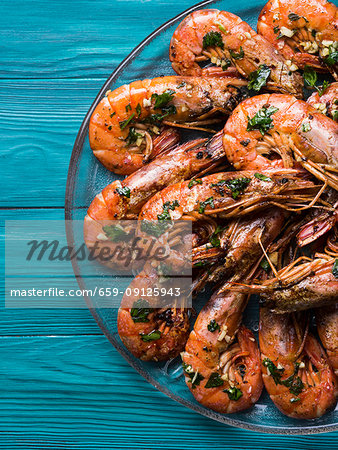 Grilled shrimps served on a dish with olive oil, parsley and garlic over dark green wooden background