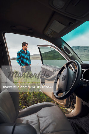 Mid adult man standing beside Dillon Reservoir, view through parked car, Silverthorne, Colorado, USA