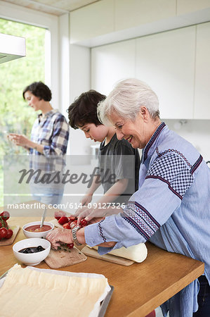 Grandmother and grandson preparing food in kitchen, mother in background