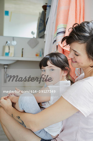 Mother and daughter sitting together in bathroom, smiling