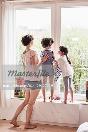 Mother, son and daughter at home, looking out of window, rear view Mother, son and daughter at home, looking out of window, rear view