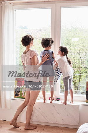 Mother, son and daughter at home, looking out of window, rear view