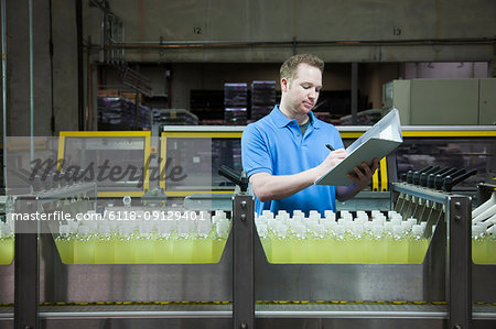 Caucasian male worker checking inventory next to a conveyor belt of lemon flaored water in a bottling plant.