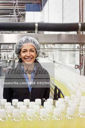 Portrait of an African American female management person standing next to a conveyor belt of lemon flavoured water in a bottling plant.